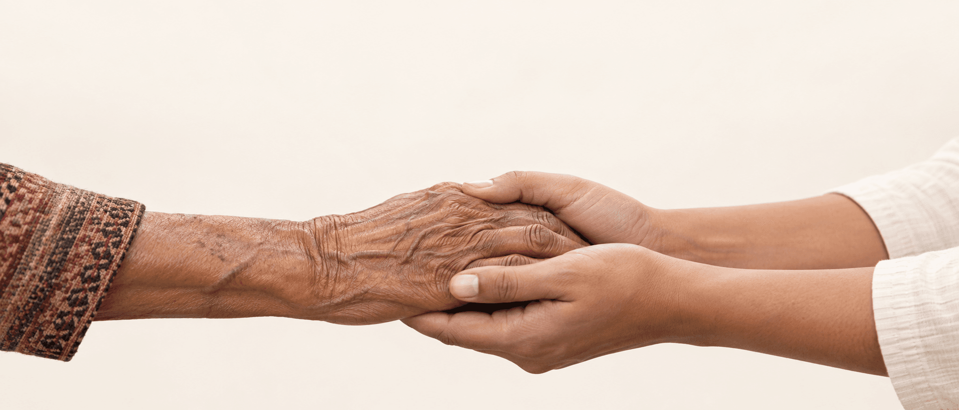An older Nepali family member's hand held gently by a younger caregiver